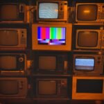 A collection of vintage televisions featuring static and color test patterns on the screens.