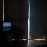 A dimly lit living room with static on the TV and curtains drawn, creating a moody atmosphere.