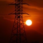 Stunning silhouette of an electric tower against an intense sunset sky with visible power lines.