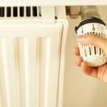 Close-up of hand adjusting radiator thermostat to control home heating temperature.
