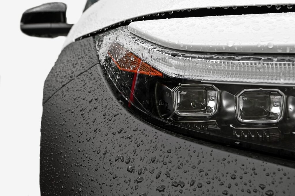 Detailed close-up of a car headlight with raindrops on the surface, showcasing modern design.