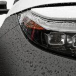 Detailed close-up of a car headlight with raindrops on the surface, showcasing modern design.