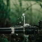 A detailed view of a leaking water pipe in a lush green garden setting.