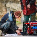 Two technicians working on a red HÜTTENBERG power generator outdoors.