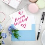 Celebratory birthday setup with a card, flowers, and coffee on a desk.