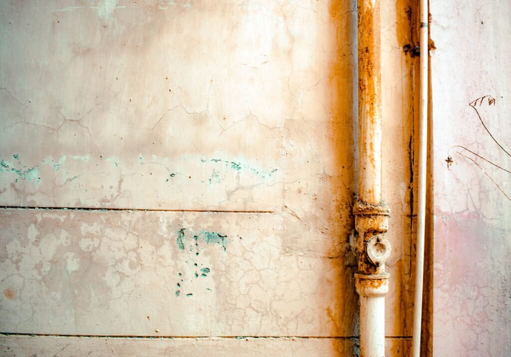 Close-up of a rusty pipe on a cracked, weathered wall in rustic tones.