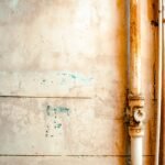 Close-up of a rusty pipe on a cracked, weathered wall in rustic tones.