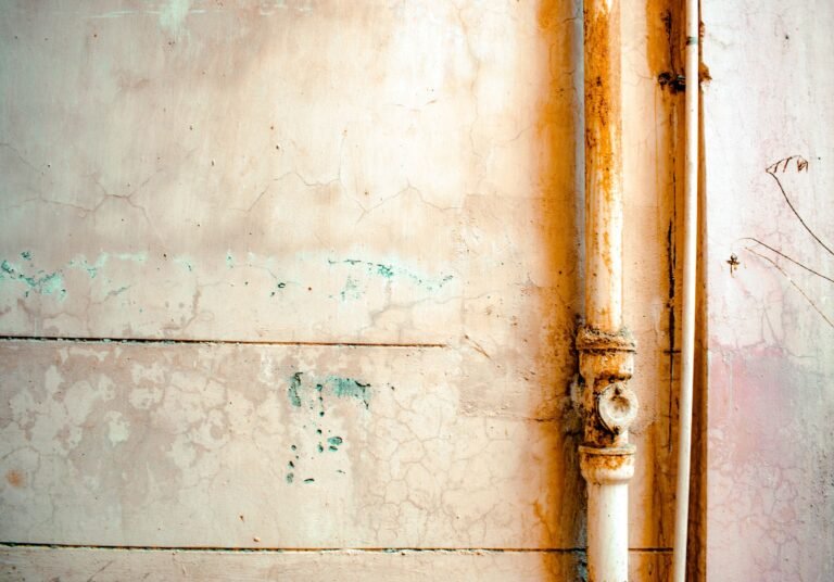 Close-up of a rusty pipe on a cracked, weathered wall in rustic tones.