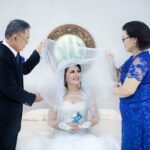 Bride with family in a joyful wedding moment, surrounded by floral decor indoors.
