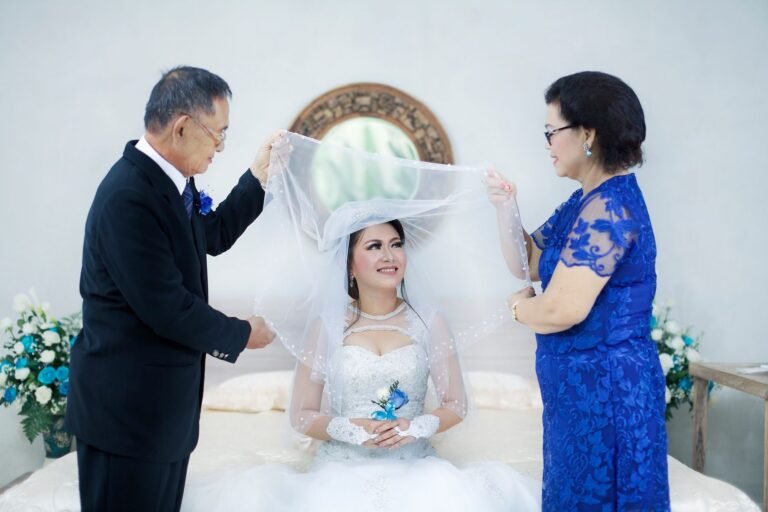 Bride with family in a joyful wedding moment, surrounded by floral decor indoors.