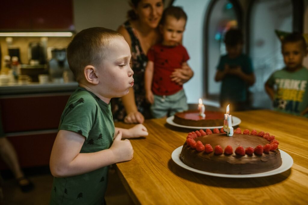 Young boy celebrating birthday by blowing candles on chocolate cake with raspberries.