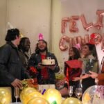 A joyful birthday party with friends, cake, and confetti indoors.