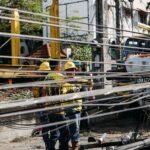 Utility workers repairing downed power lines amidst damaged infrastructure. Outdoor setting with chaos.