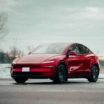 Red electric car parked outdoors, showcasing sleek design amidst winter scenery.