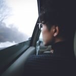 Side view of a thoughtful person with eyewear gazing out of a car window into a foggy winter landscape.