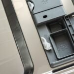 Closeup of an open dishwasher detergent compartment with water droplets visible.