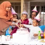 Children celebrating a birthday with cake and party hats, surrounded by friends and family.