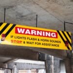 A prominent warning sign in a UK car park advises drivers to stop if lights flash and horn sounds.