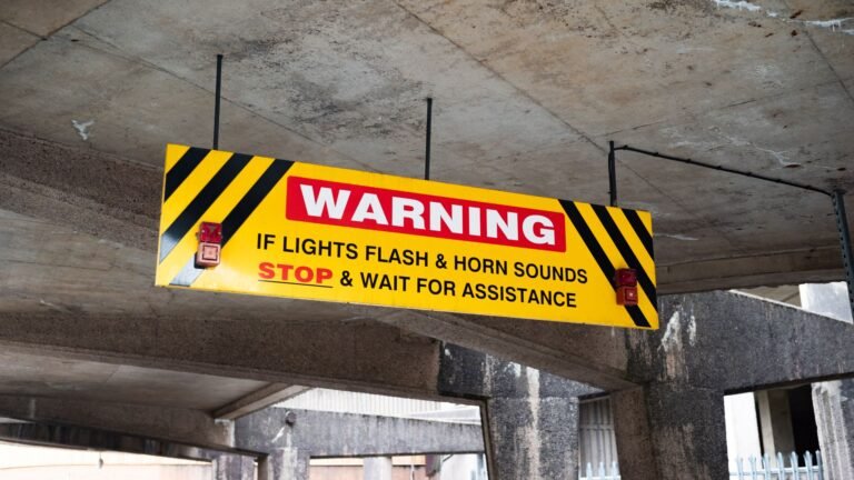 A prominent warning sign in a UK car park advises drivers to stop if lights flash and horn sounds.