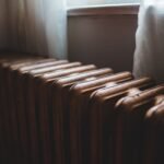 Aged heating battery made of cast iron near windowsill with curtains in house