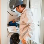 Man pouring liquid detergent into a stacked washer and dryer in a modern laundry room.