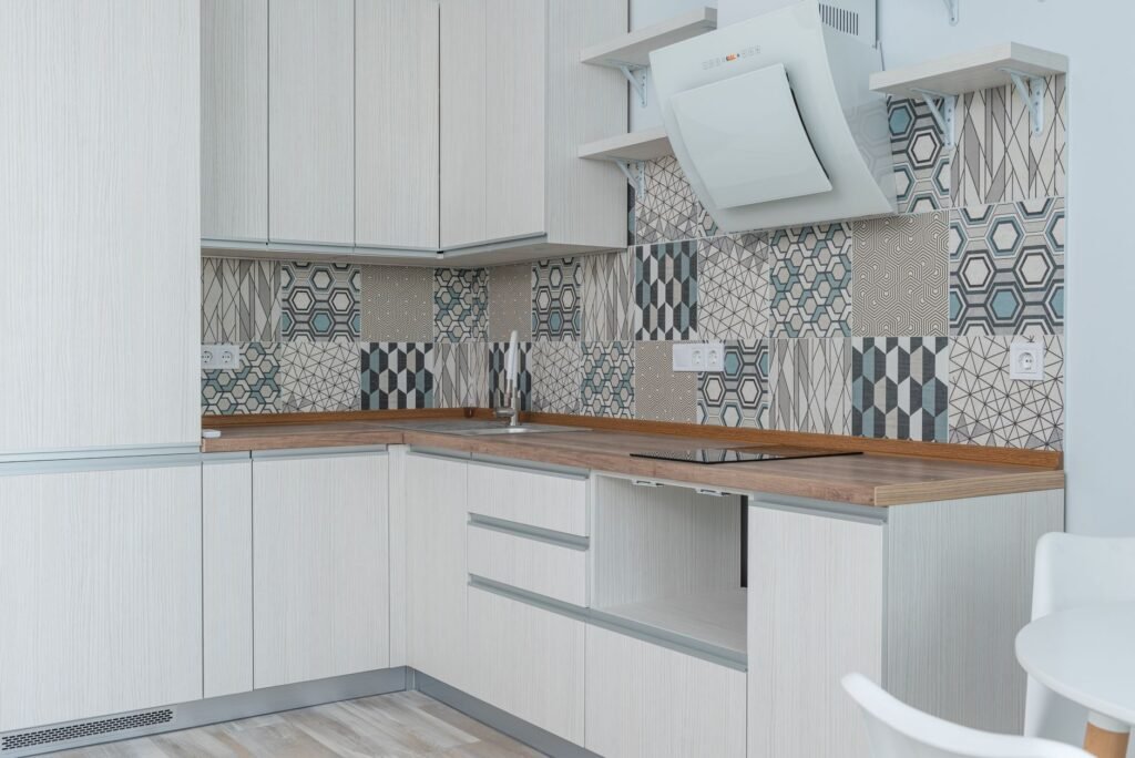 Interior of contemporary kitchen with white cabinets and wooden counter near ornamental tile on wall and modern appliances in apartment