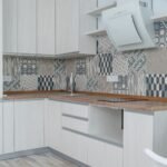 Interior of contemporary kitchen with white cabinets and wooden counter near ornamental tile on wall and modern appliances in apartment