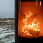 Indoor fireplace with burning flame creating warmth against snowy winter outdoors.