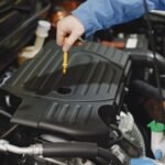 Close-up of a person checking engine oil using a dipstick in a car's engine bay.
