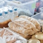 Plastic-wrapped food items and bottled water organized in storage containers and tin cans.