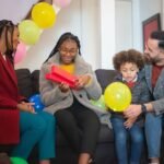 Happy family enjoying a birthday celebration with balloons, gifts, and smiles on a cozy sofa.