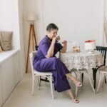 A senior woman gracefully celebrates her birthday in a stylish indoor setting with cake and tea.