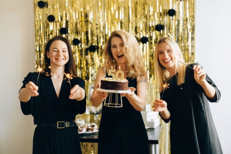 Happy women celebrating a 50th birthday with cake and sparklers indoors.