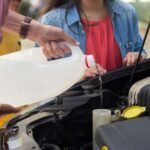 Close-up of a person pouring windshield washer fluid into a car, emphasizing vehicle maintenance.