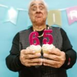 Senior man holding cupcakes with 65 candle during his birthday celebration.