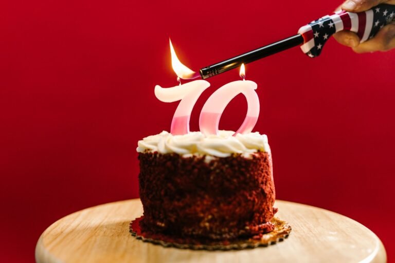 A close-up of a birthday cake with '70' candles being lit against a red background.