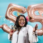 Smiling woman celebrates 55th birthday with balloons and festive decor.