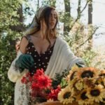 A woman in a polka dot dress harvests sunflowers in a sunlight-dappled garden.
