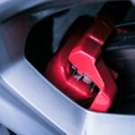 Detailed photo of a red automotive brake caliper and disc brake in focus.