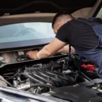 Auto mechanic performs engine maintenance on a car. Focus on hands and engine components.