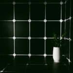 A minimalist scene featuring a green plant in a white vase against a dark tiled wall.