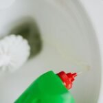 Top view of liquid detergent pouring from green plastic bottle in toilet bowl with toilet brush