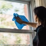 A woman cleans a window using a blue microfiber cloth providing a streak-free shine.